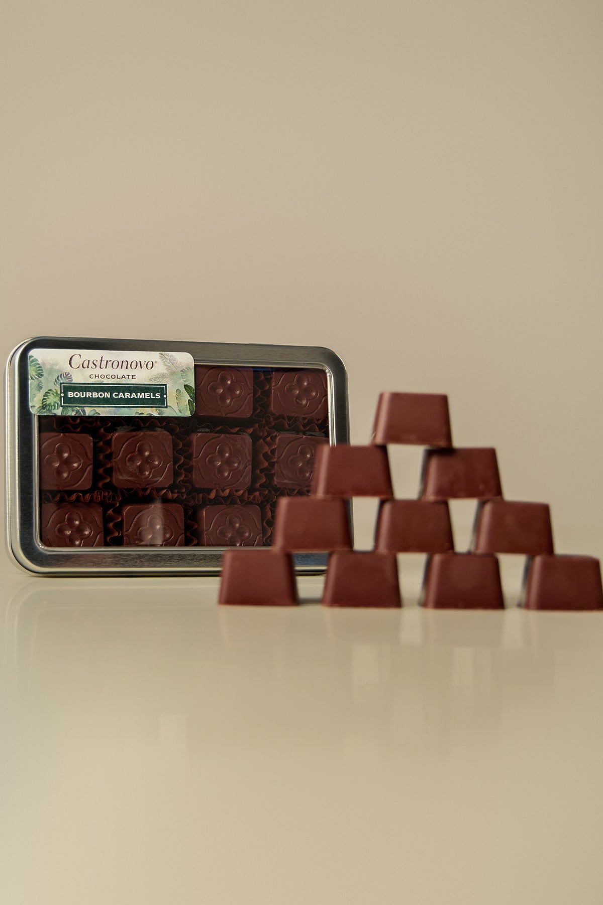 A tin of chocolate bonbons placed on a table with several bonbons arranged outside the tin, coated in dark chocolate and caramel.