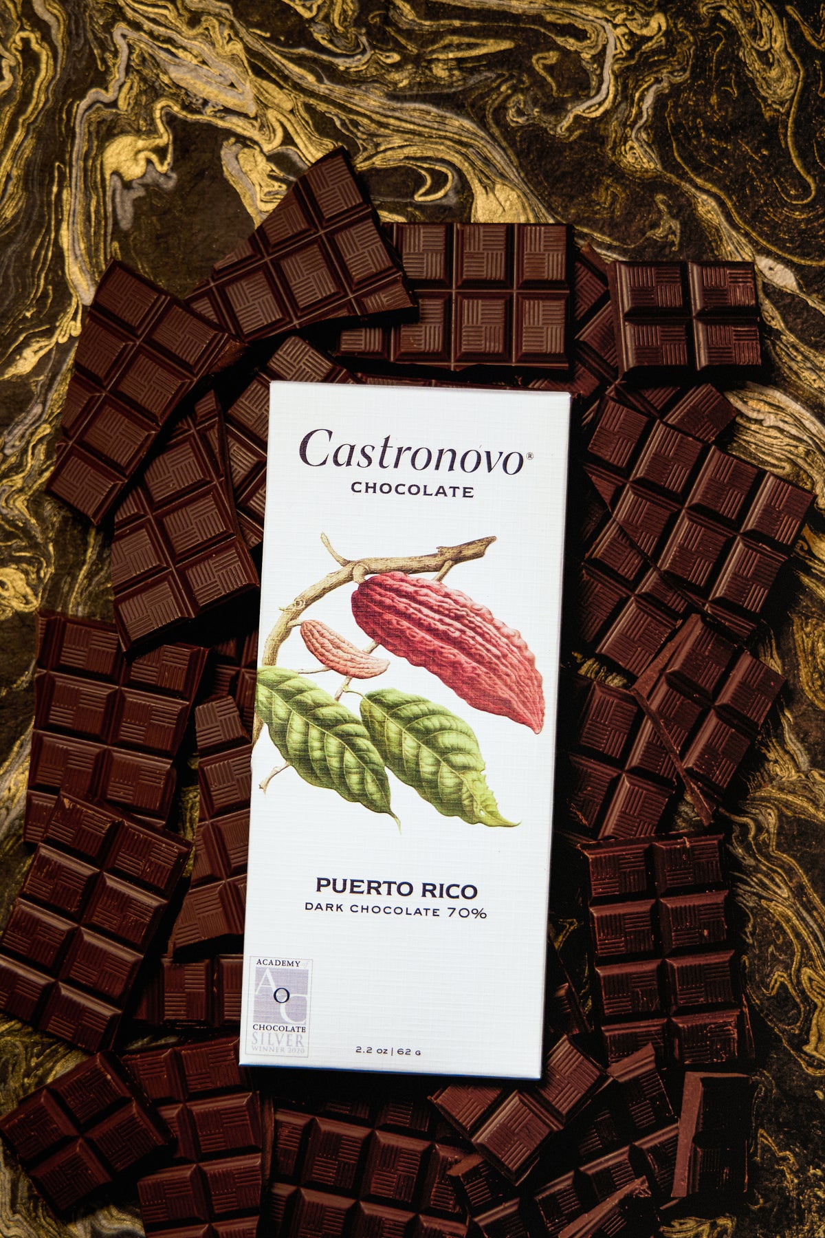 A bar of dark chocolate with the brand Castronovo Chocolate, labeled 'Puerto Rico 70% Dark', displayed on a marble surface surrounded by pieces of chocolate